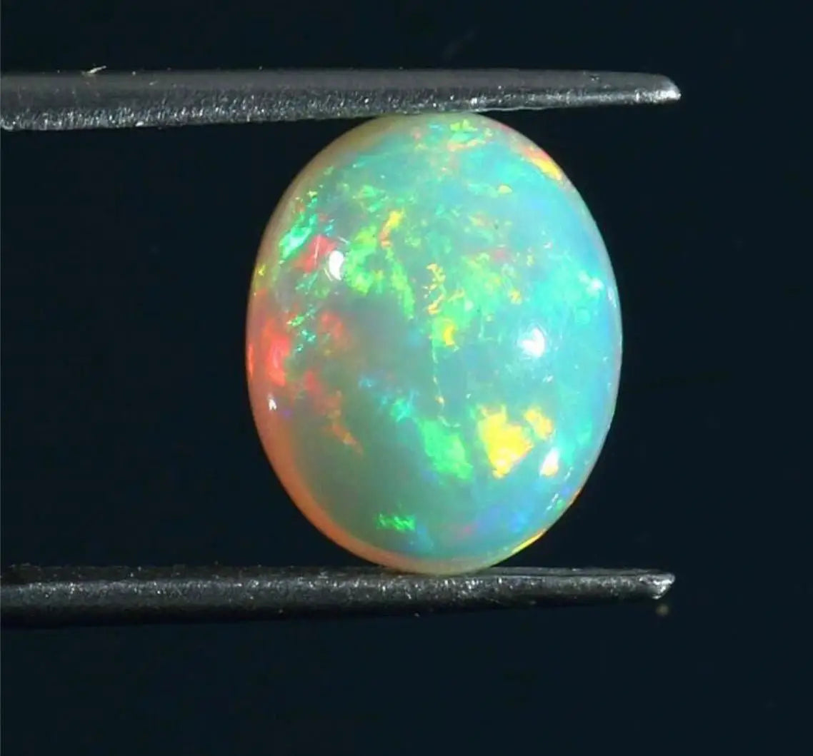 Oval opal cabochon between two metal tweezers, aqua base with green fire.