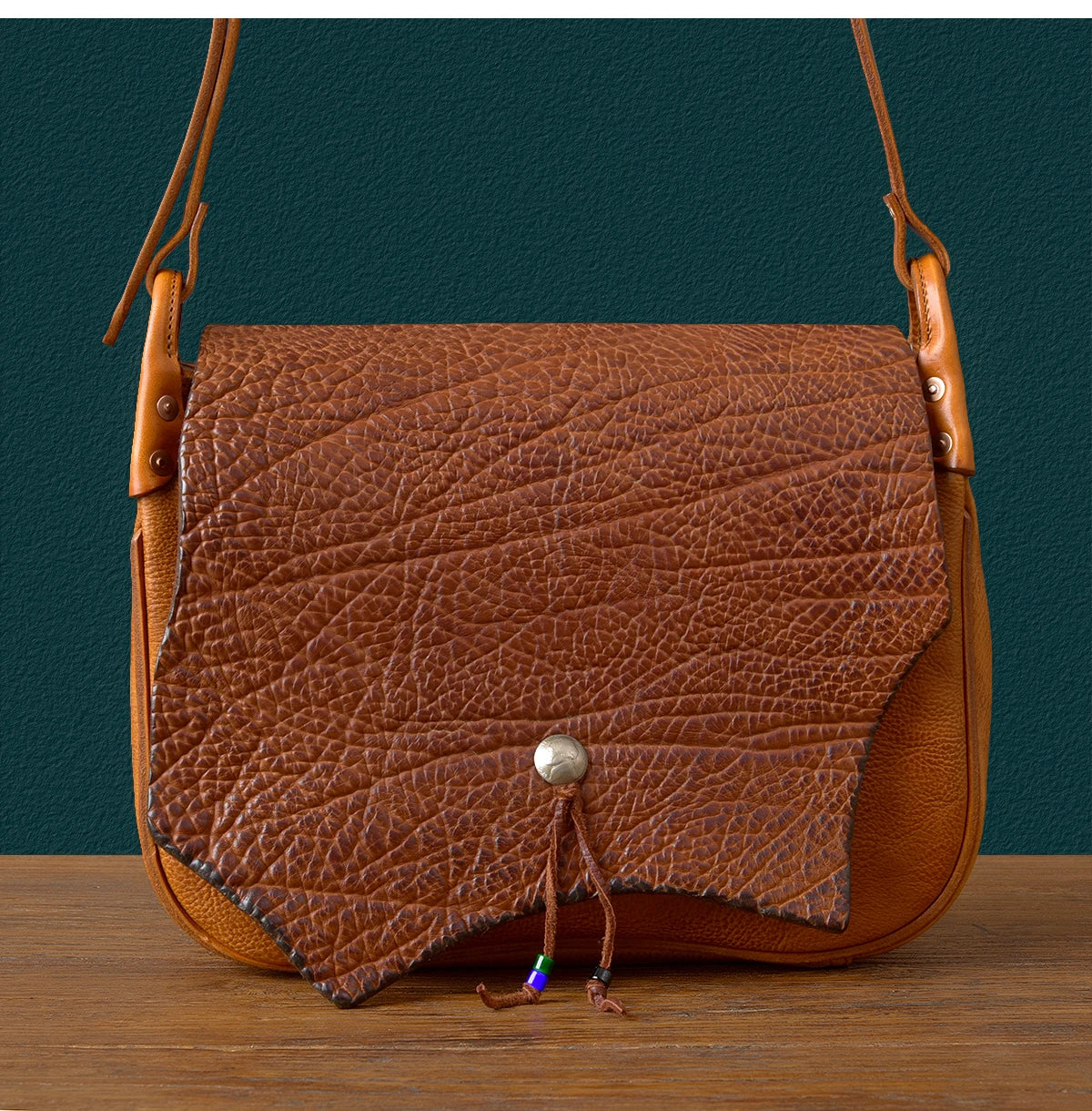 Vintage handmade brown cowhide leather messenger bag with textured flap, silver snap button, and decorative bead detail.