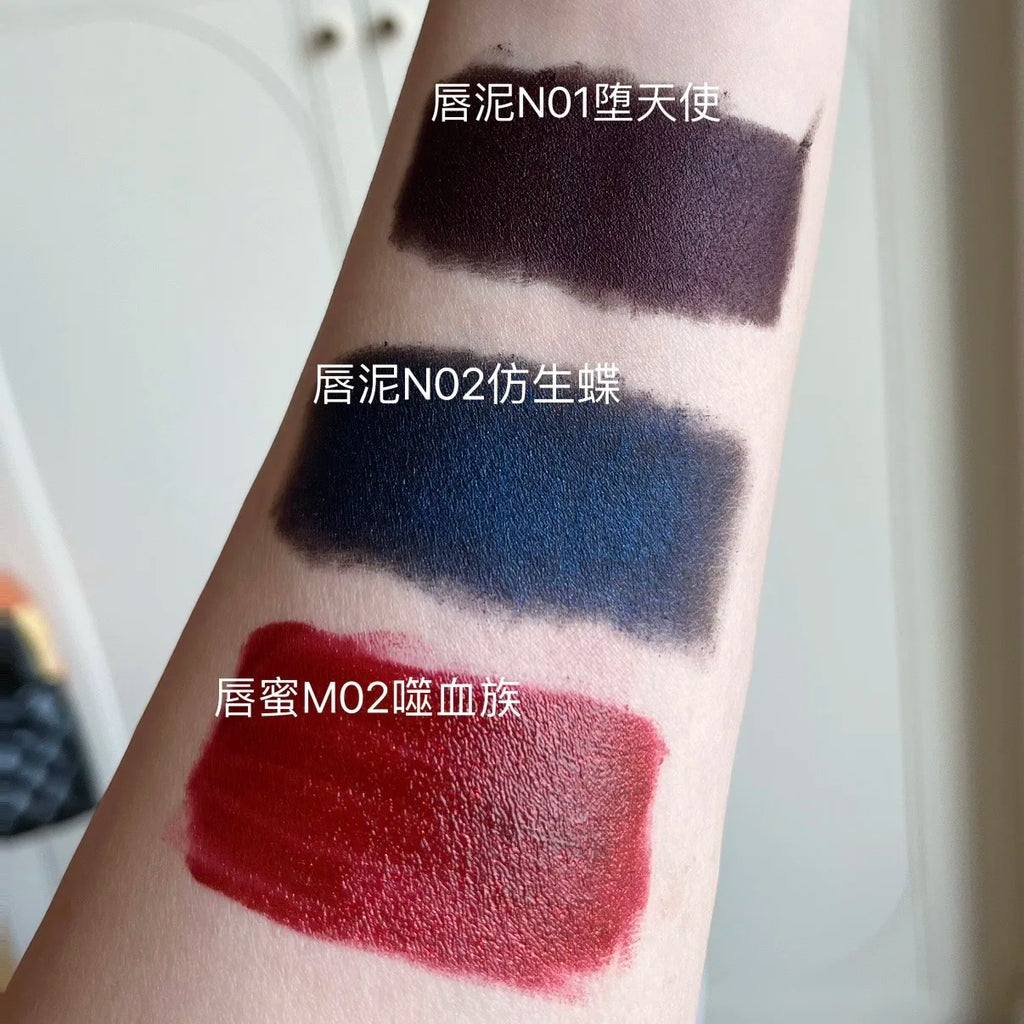 DE'LANCI gothic lip swatches: matte dark purple, shimmer dark blue lip mud, and glossy red mirror lip finish on arm.