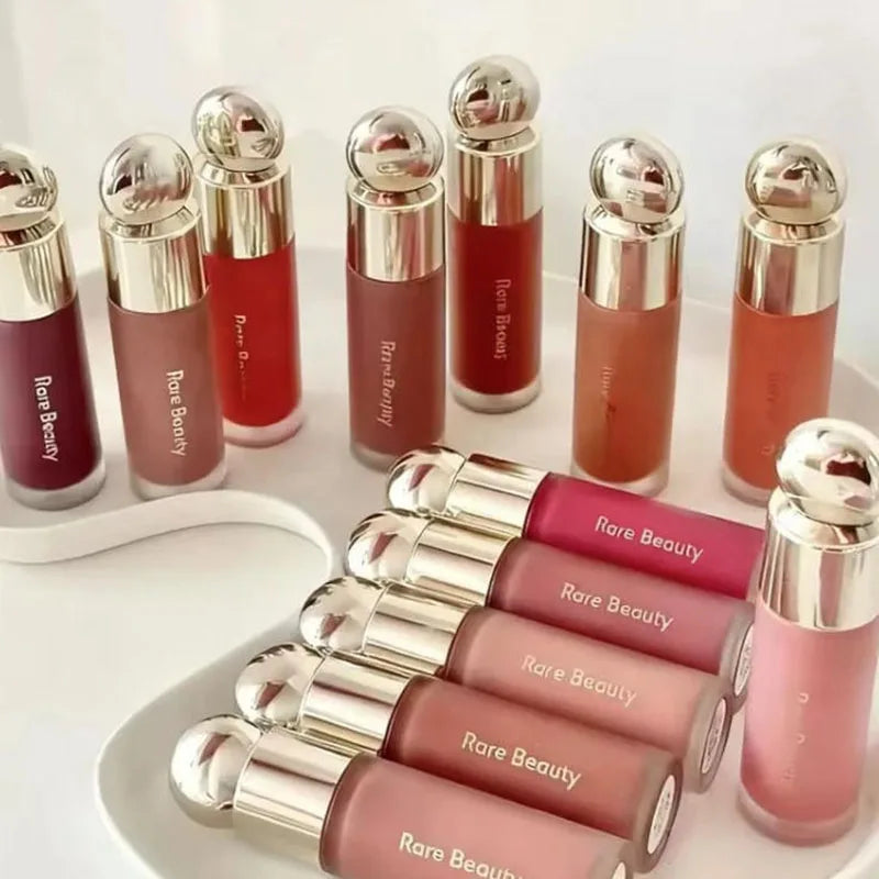 Rare Beauty Soft Pinch liquid blush collection in various shades with gold caps arranged on a white tray.