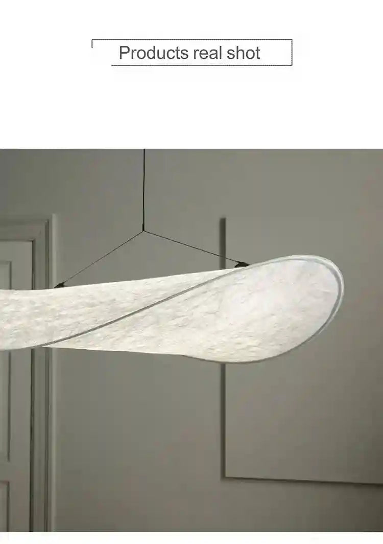 Long, curved white fabric pendant lamp with a textured, paper-like finish, suspended by thin black wires.