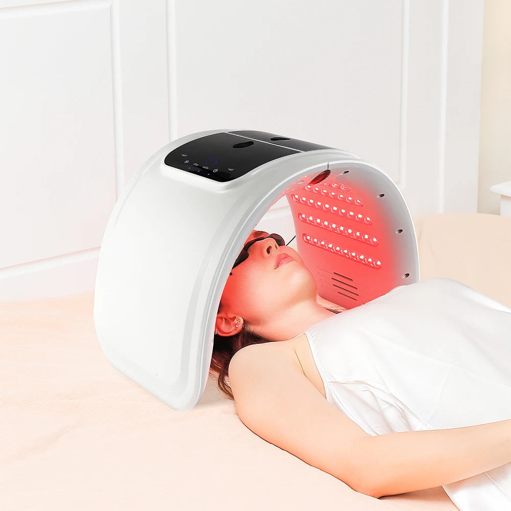 White curved LED facial light therapy device with red lights over a person wearing protective eyewear.