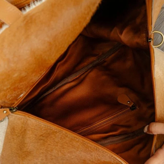 Tan genuine leather western duffel trunk with brown fabric interior lining, zipper pockets, and tassel accents.