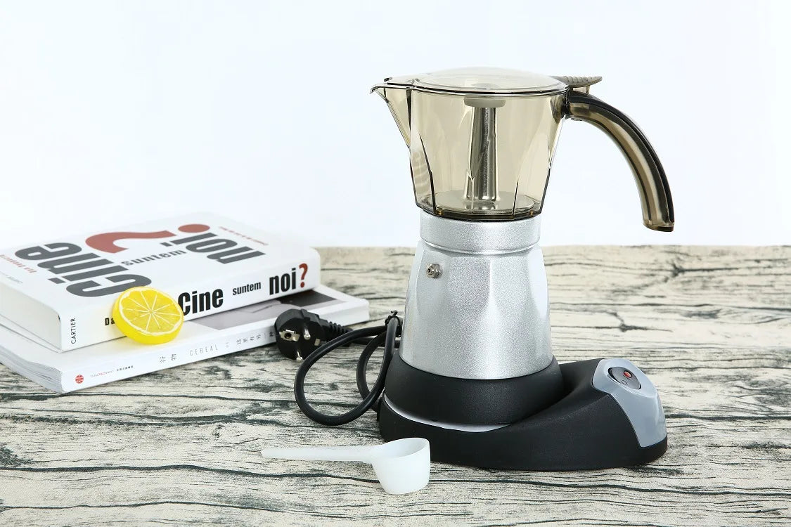 Electric moka pot with silver metal base, transparent brown top, and black power stand on a wood-grain table.