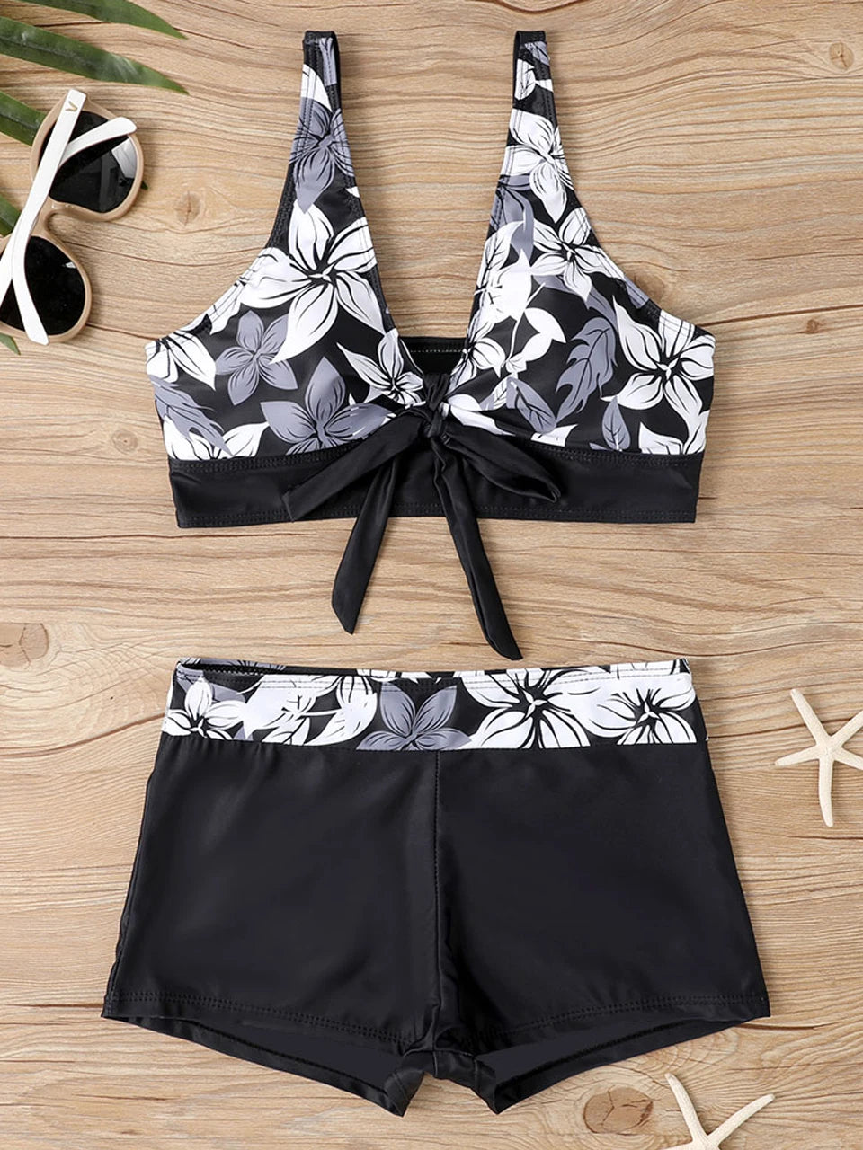 Tidesmit black and white floral print high-waisted bikini with a knotted sports-style top on a wooden background.