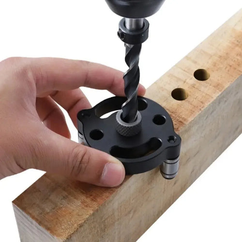 Black vertical drilling locator jig clamped to a wooden board while a drill bit bores a hole