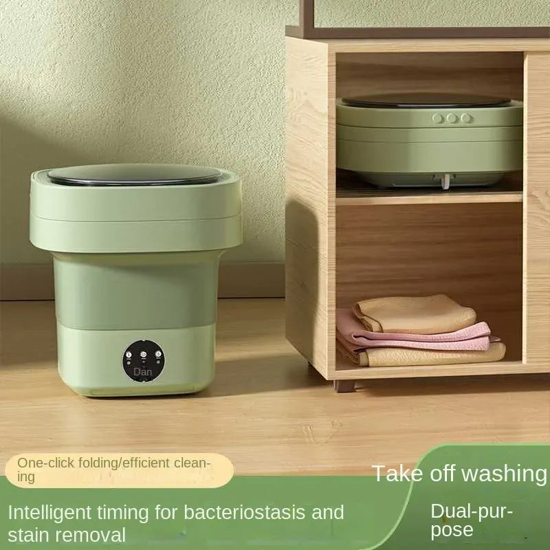 Portable folding washing machine in green, shown standing on a floor and folded inside a wooden cabinet shelf.