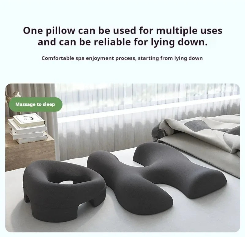 Two dark grey, contoured foam spa pillows for facial and chest support, placed on a white surface by a window.