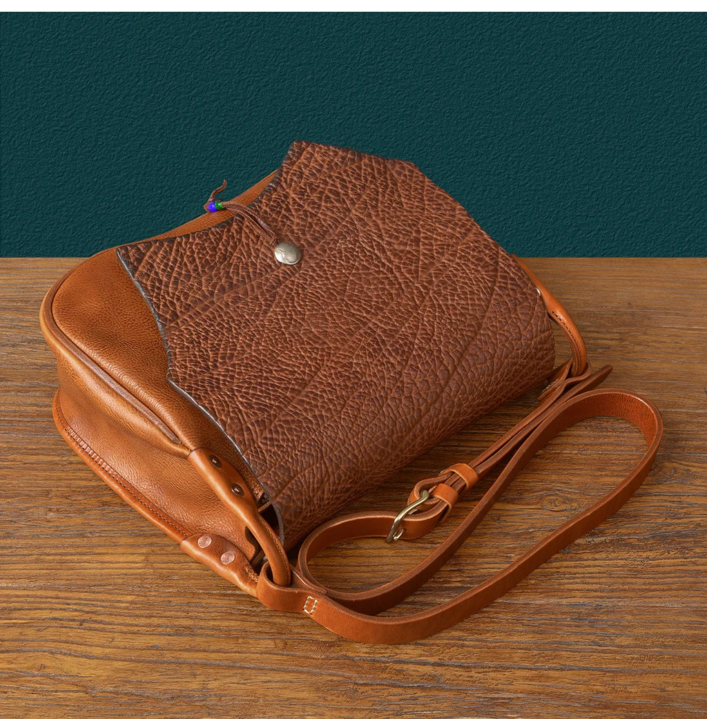 Vintage brown genuine cowhide messenger bag with textured flap, adjustable shoulder strap, and artisanal rivet details.