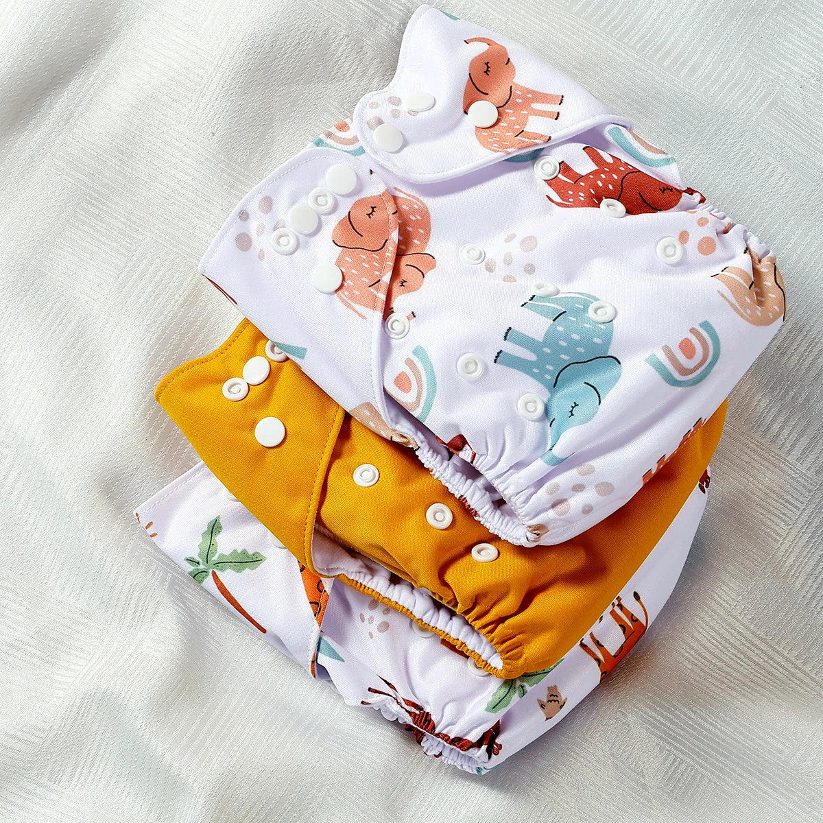 Reusable cloth baby diapers with adjustable snap buttons in elephant, palm tree, and solid yellow prints.