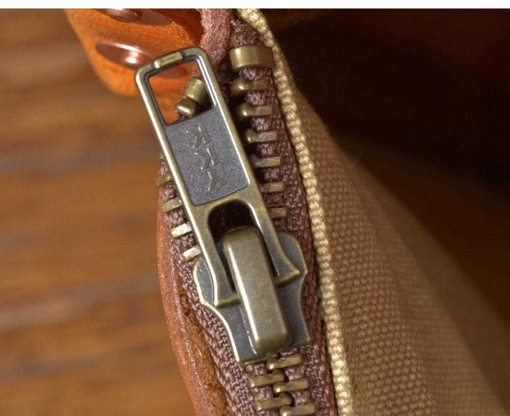 Close-up of a vintage luxury messenger bag in tan cowhide leather with a durable YKK brass zipper and canvas lining.
