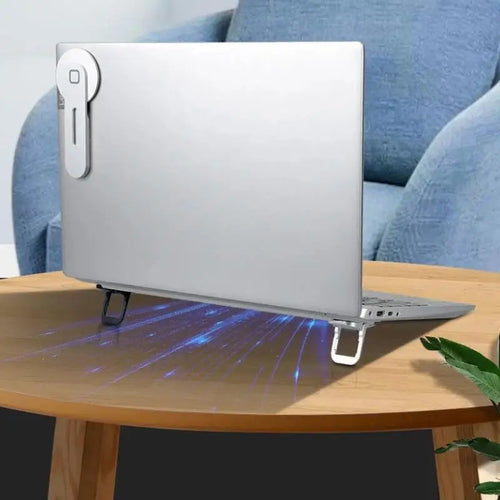 Silver laptop on a wooden table, elevated by two small, foldable metallic supports with a blue light cooling effect.