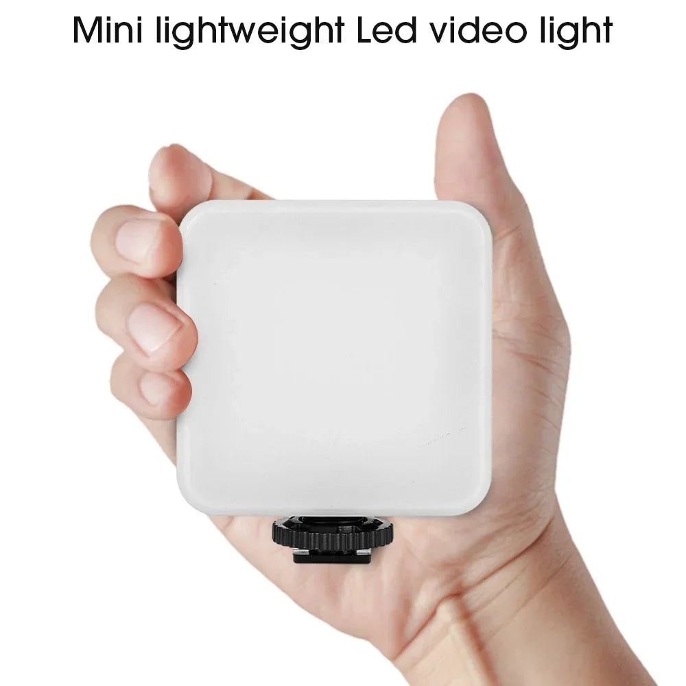 Small, square white LED video light with a black bottom mount, held in an open hand for photography and vlogging.
