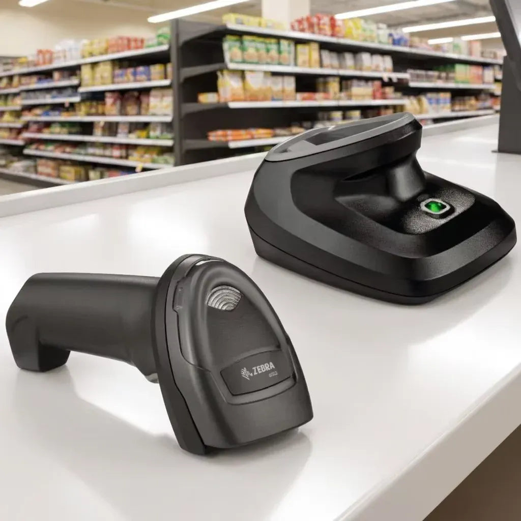 Black handheld barcode scanner placed on countertop beside charging cradle