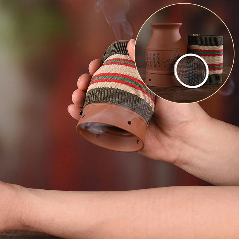 Handheld ceramic moxibustion burner with striped fabric wrap, emitting smoke, with a mesh insert visible in an inset.