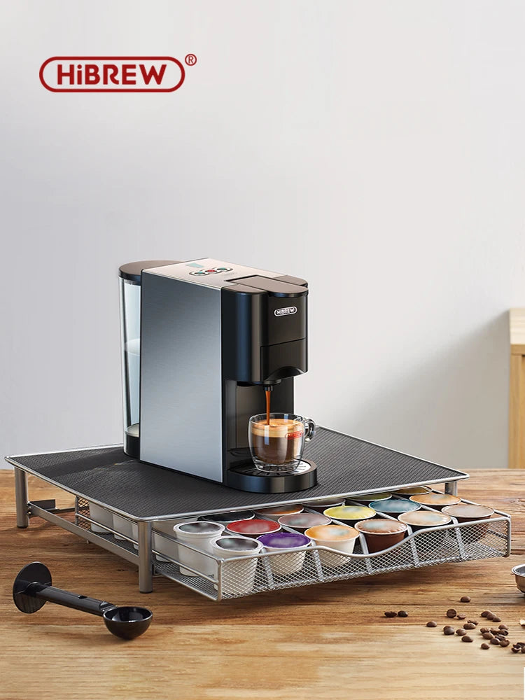 HiBREW capsule coffee machine in black and silver on a metal pod storage drawer stand, brewing into a glass mug.