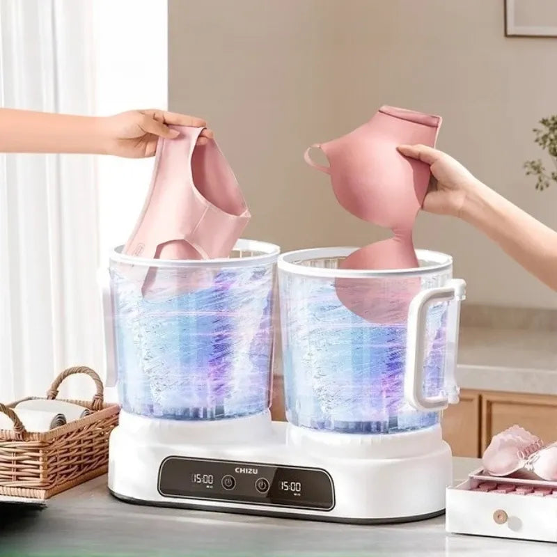 Portable mini washing machine cleaning pink undergarments in dual transparent tubs with a digital timer display.