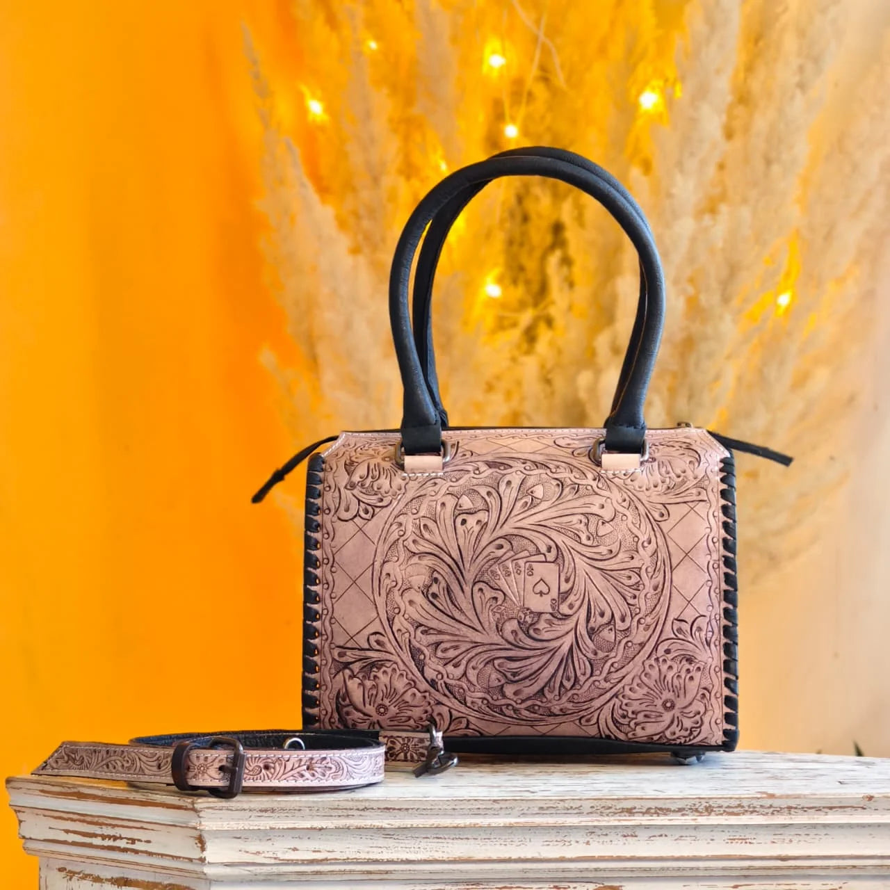 Luxury hand-tooled floral leather trunk bag with black handles and spade card detailing. Stylish designer duffle.