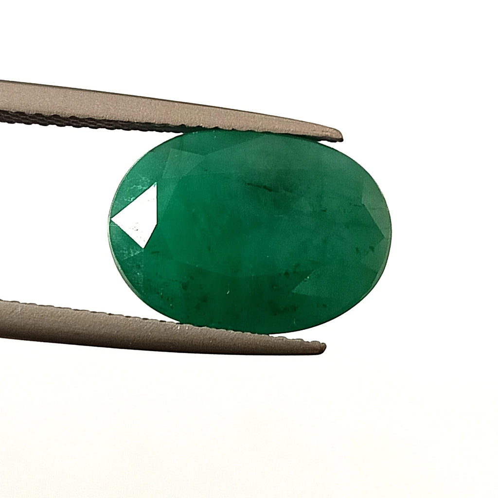 Oval green emerald gemstone, faceted loose cut, held between metal tweezers
