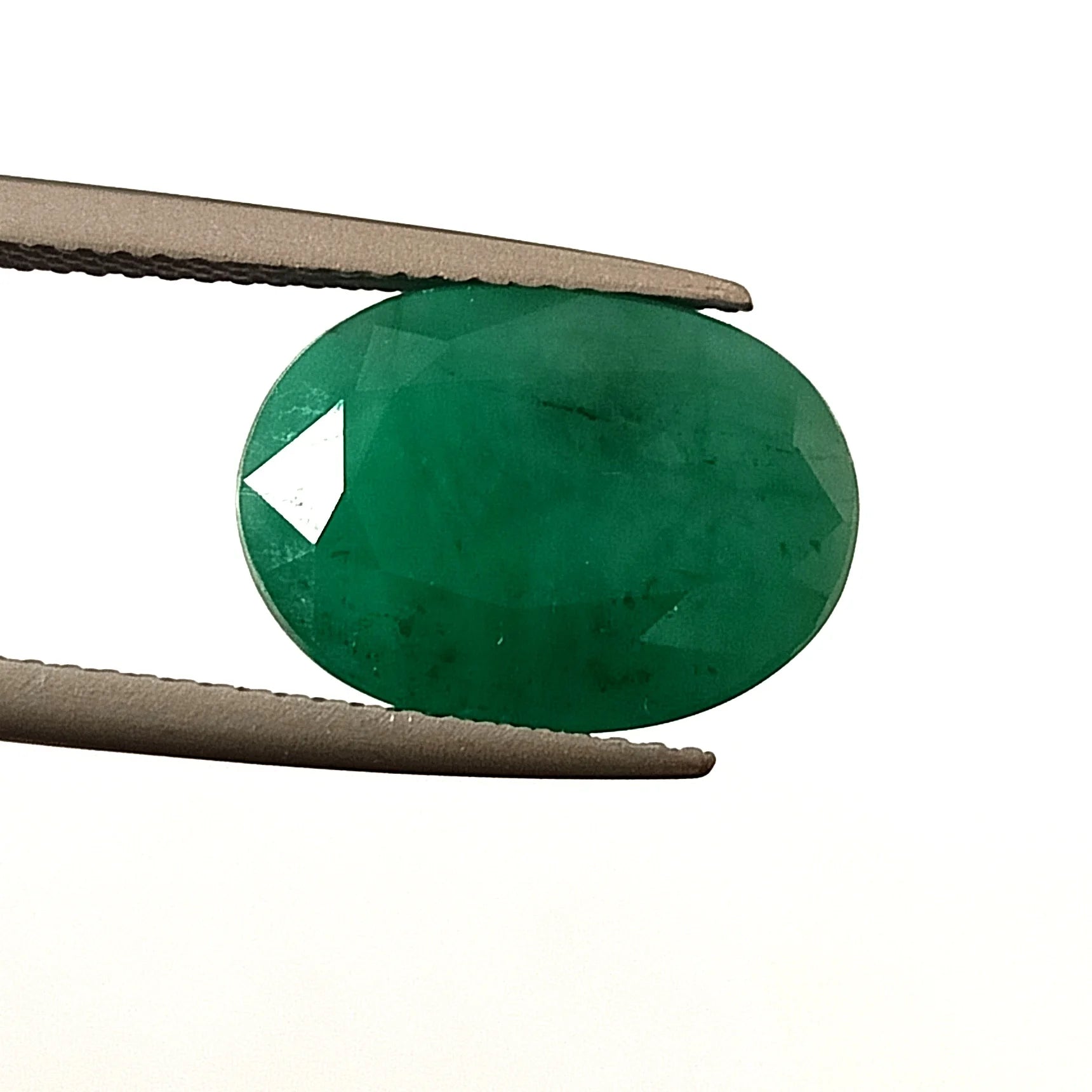 Oval green emerald gemstone, faceted loose cut, held between metal tweezers