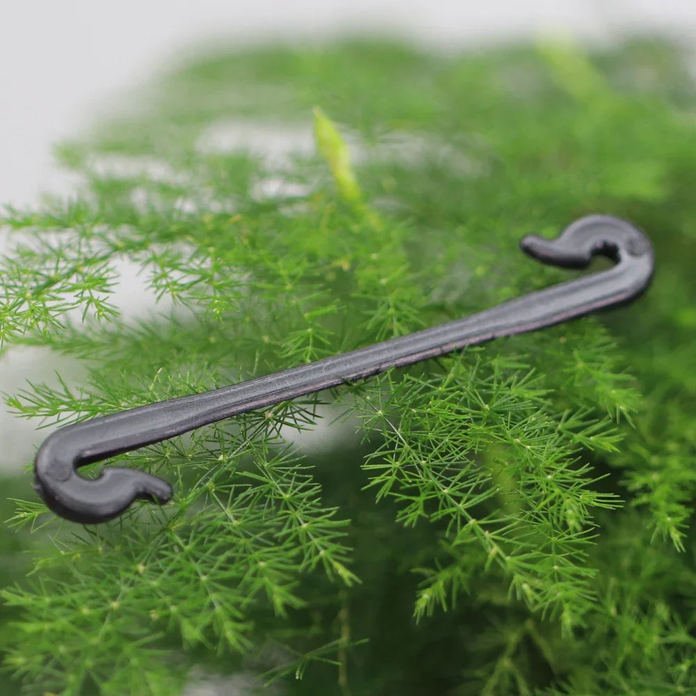 Black plant support hook lying on green grass