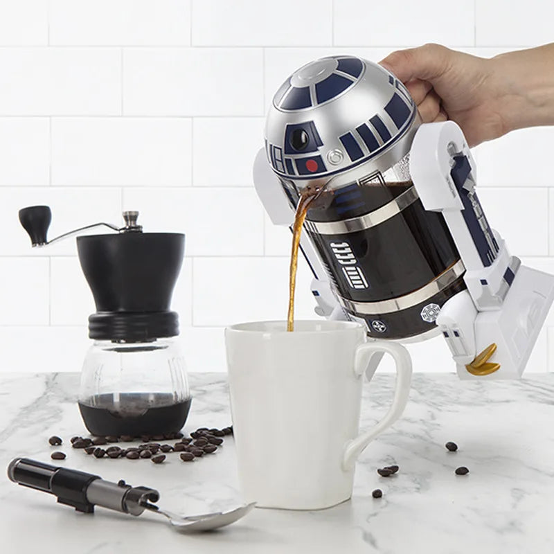 Star Wars R2-D2 glass and plastic French press coffee maker pouring coffee into a white mug on a marble counter.