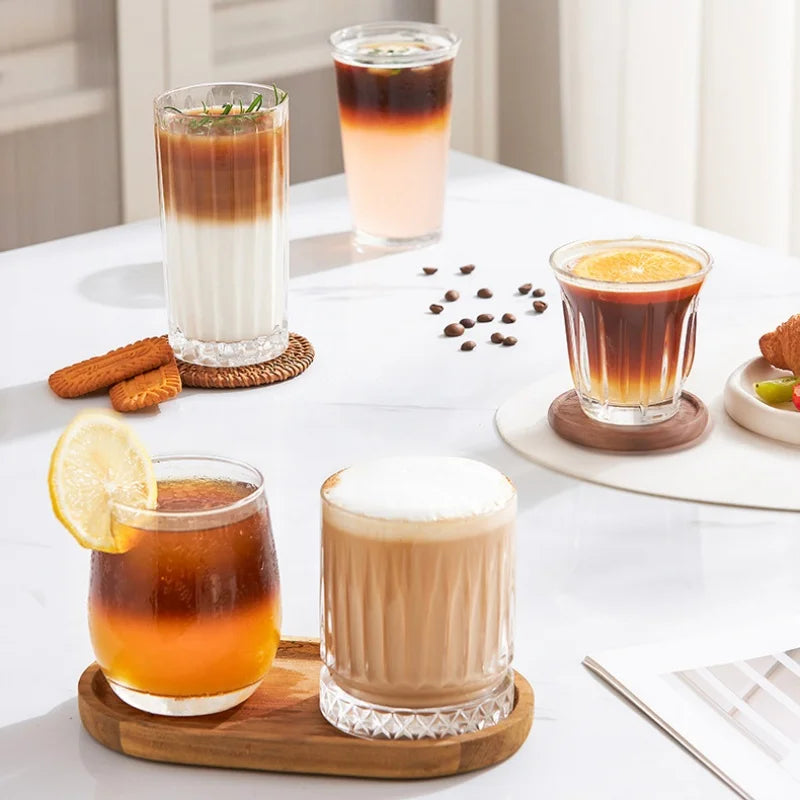 Set of clear glass fluted coffee cups for iced lattes and espresso on a wooden tray and coasters.
