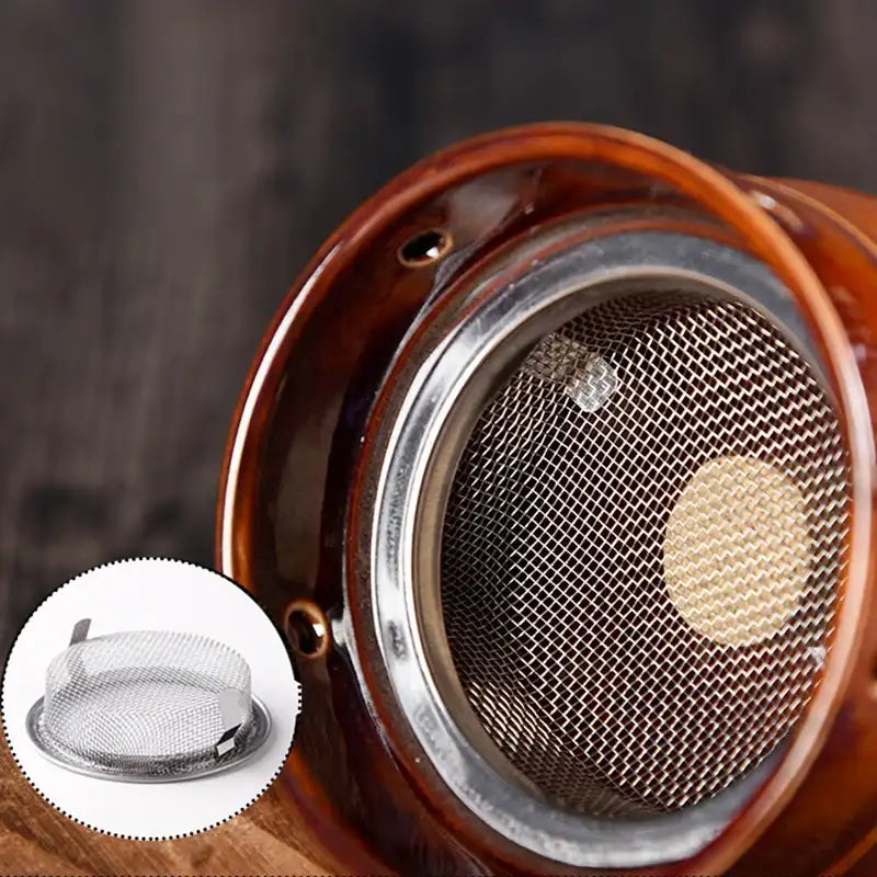Brown ceramic moxibustion cup with a circular metal mesh screen insert for therapy. Close-up, top-down view.