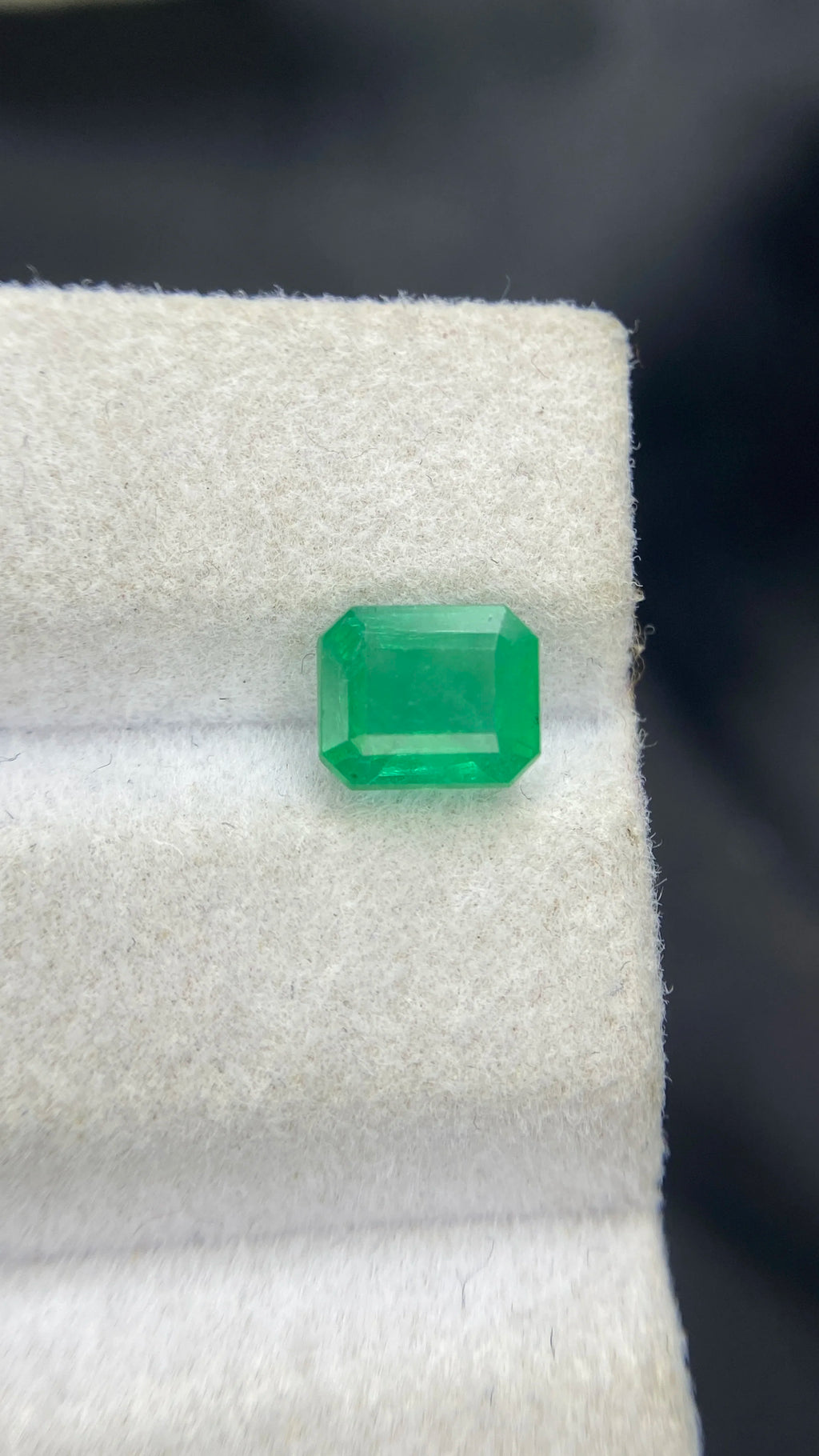 Green emerald-cut gemstone on white display pad, front view