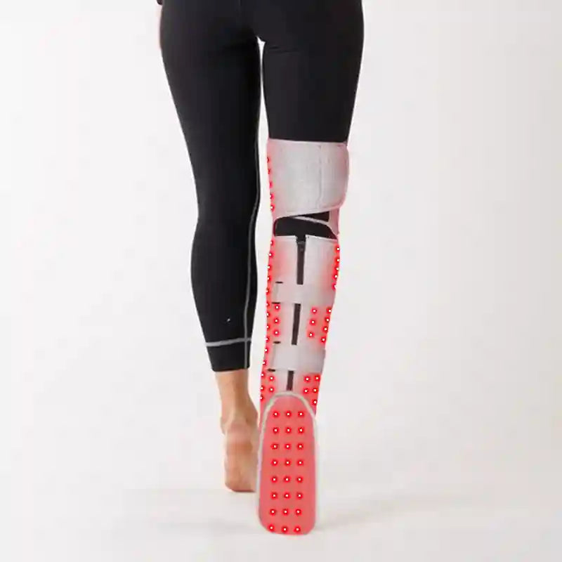 A person wearing a grey, adjustable leg heating brace with bright red LED lights for physiotherapy.