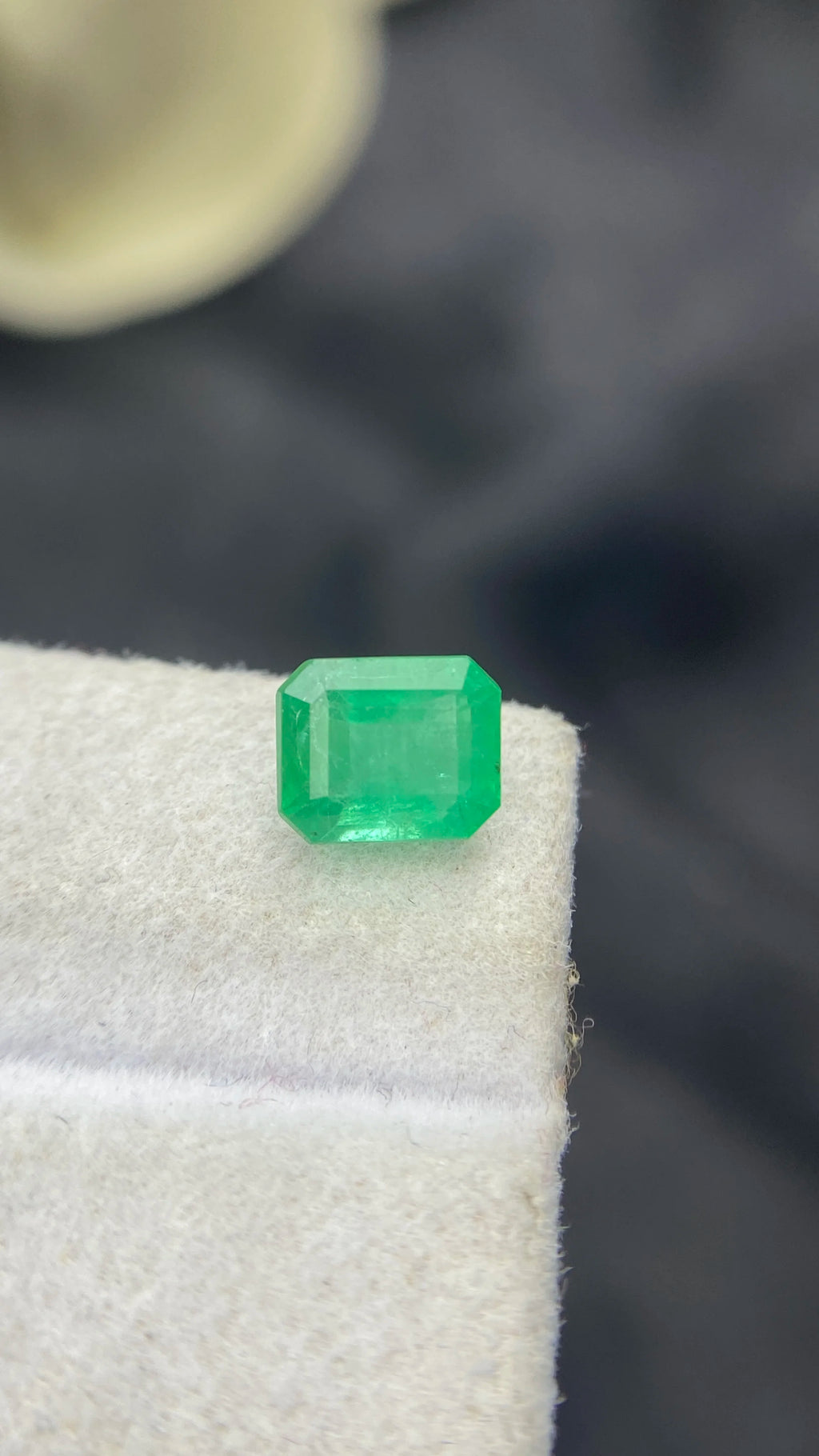 Loose green emerald-cut octagon emerald gemstone, front view on white pad