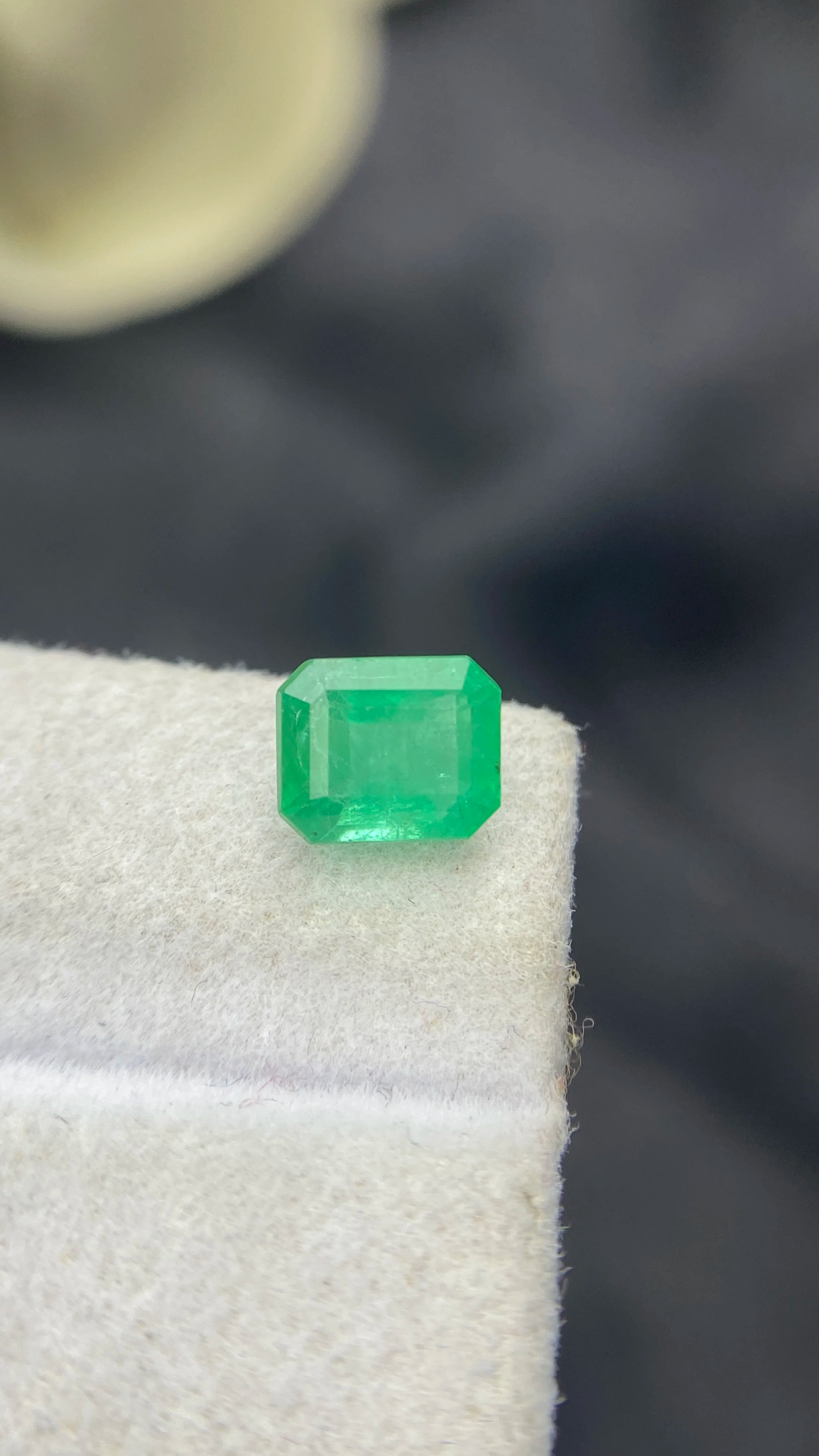 Loose green emerald-cut octagon emerald gemstone, front view on white pad