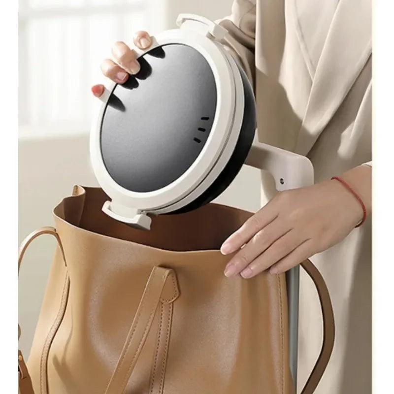 Portable electric folding hot pot unit in white with dark lid, being carried in a tote bag