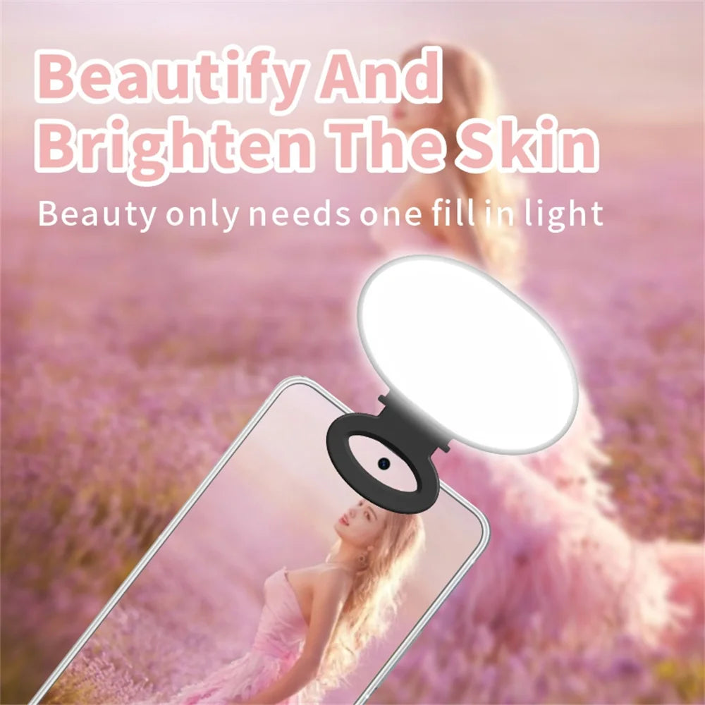 Clip-on white oval LED selfie light attached to the top of a smartphone to illuminate a person for photos.