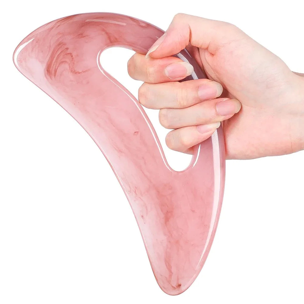 Hand holding a translucent, pink, S-shaped gua sha tool made of smooth resin for facial and body massage.
