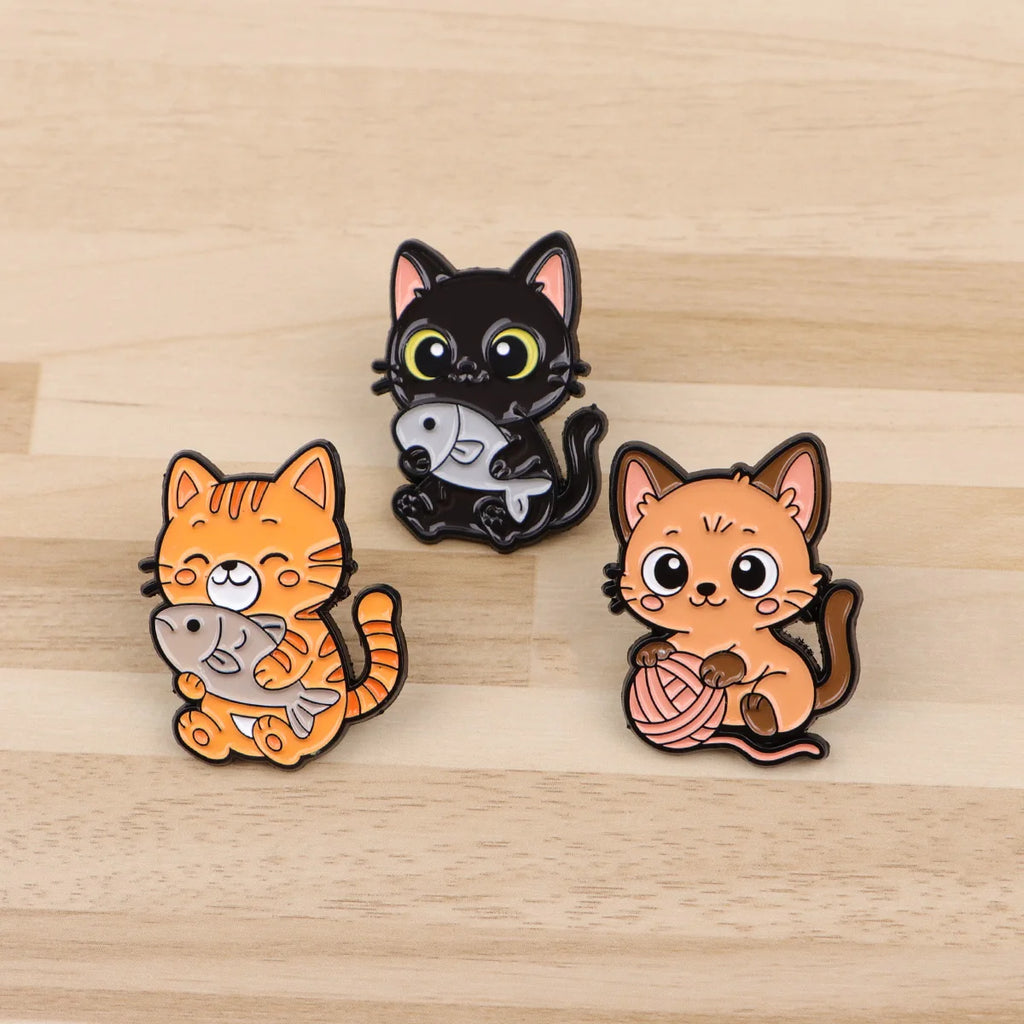 Cute cat enamel pins, featuring black and orange kittens with fish and yarn, perfect for backpacks or lapel accessories.