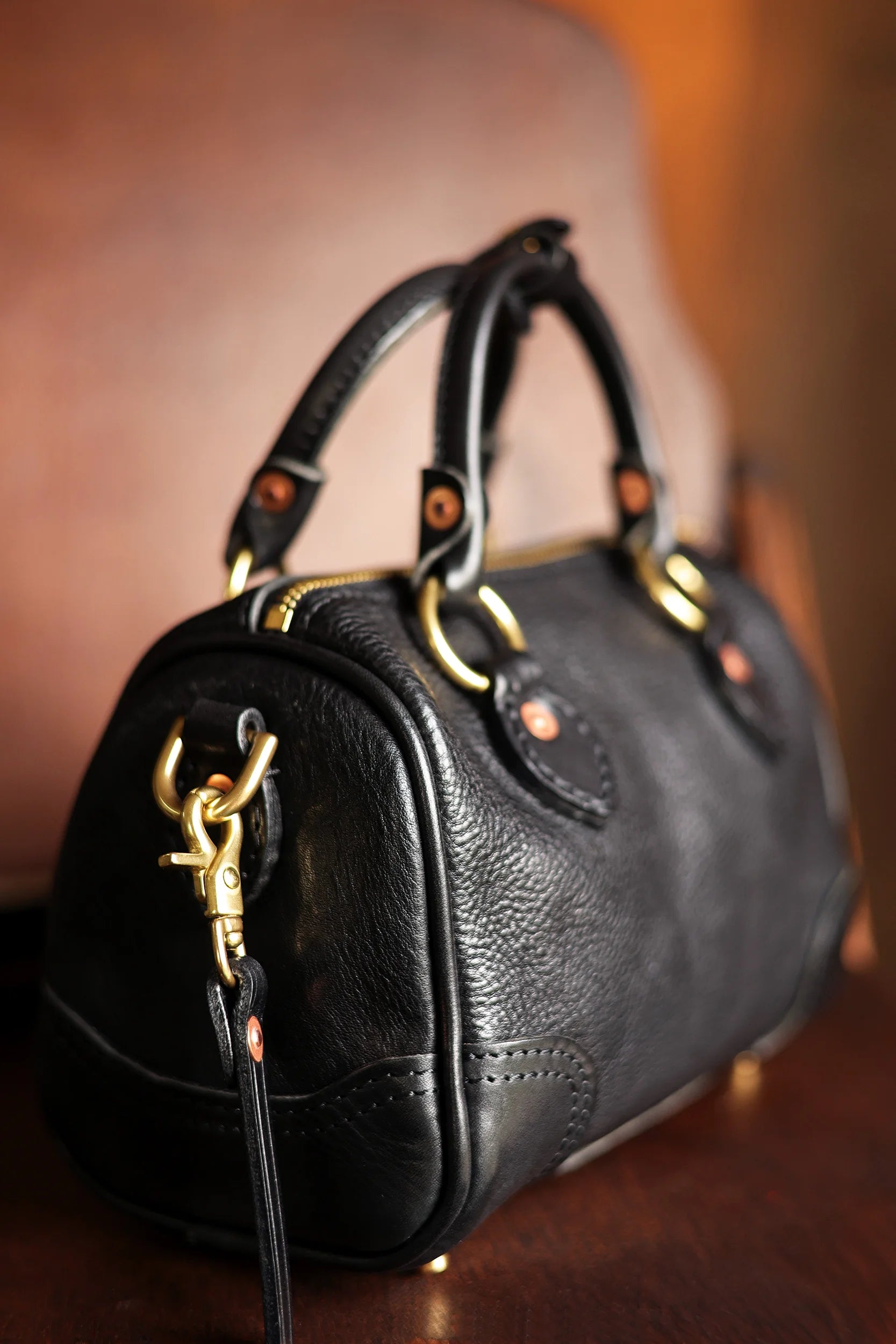 Black genuine cowhide leather small designer handbag with vintage brass hardware and top handle straps.