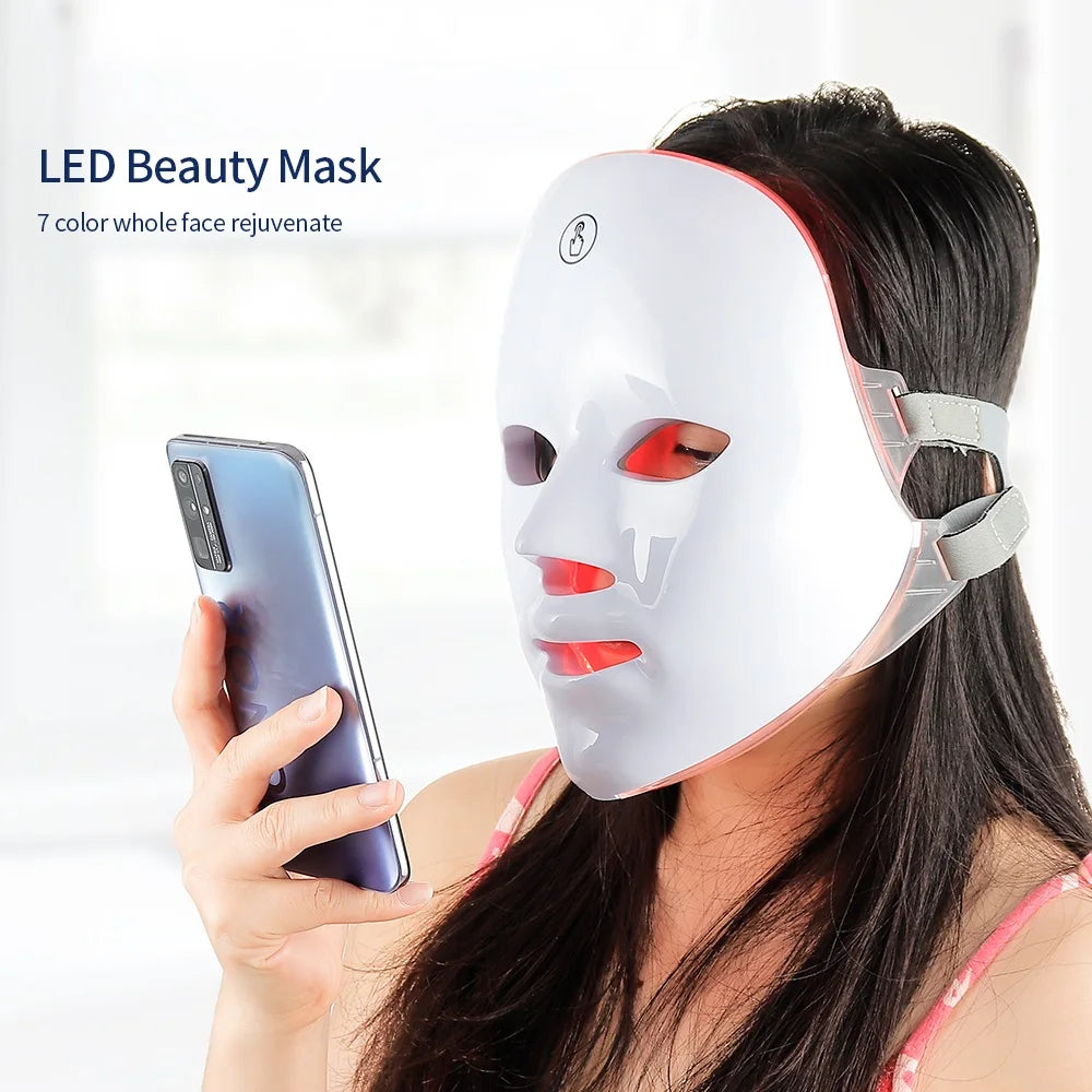 Woman wearing a sleek white LED light therapy face mask while holding a smartphone.