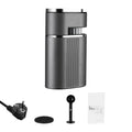Dark grey portable coffee maker with power cord, measuring scoop, and user manual on a white background.