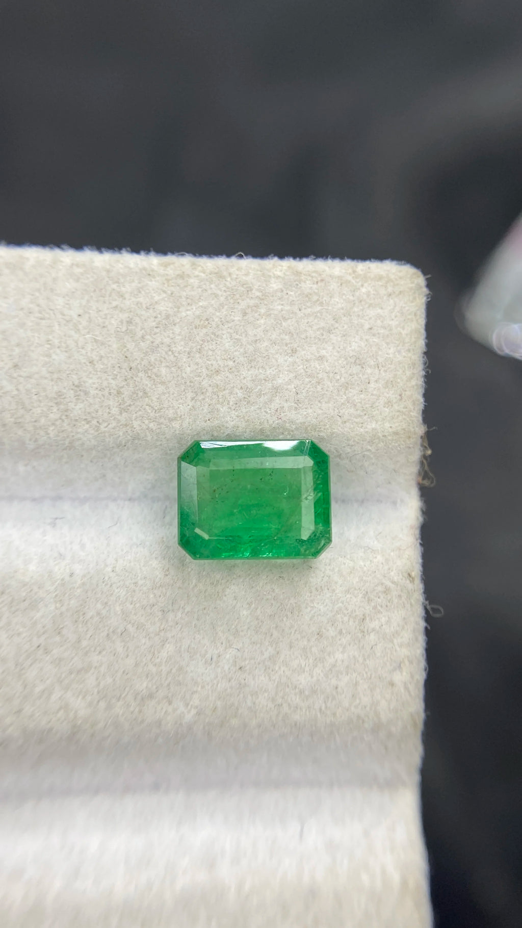 Green emerald-cut loose gemstone with stepped facets on white felt