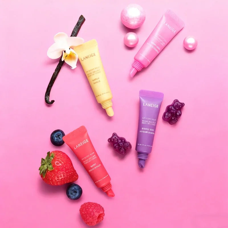 Laneige hydrating lip balm tubes in various fruit scents on pink background with strawberries, blueberries, and pearls.