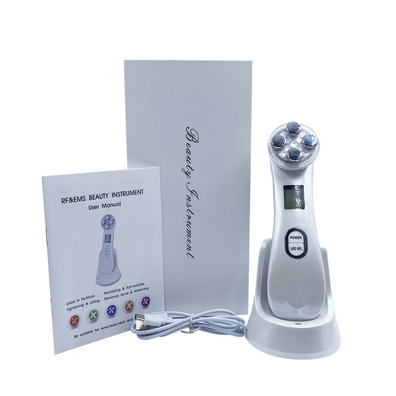 White EMS facial beauty device with charging base, manual, and USB cable against a plain white background.