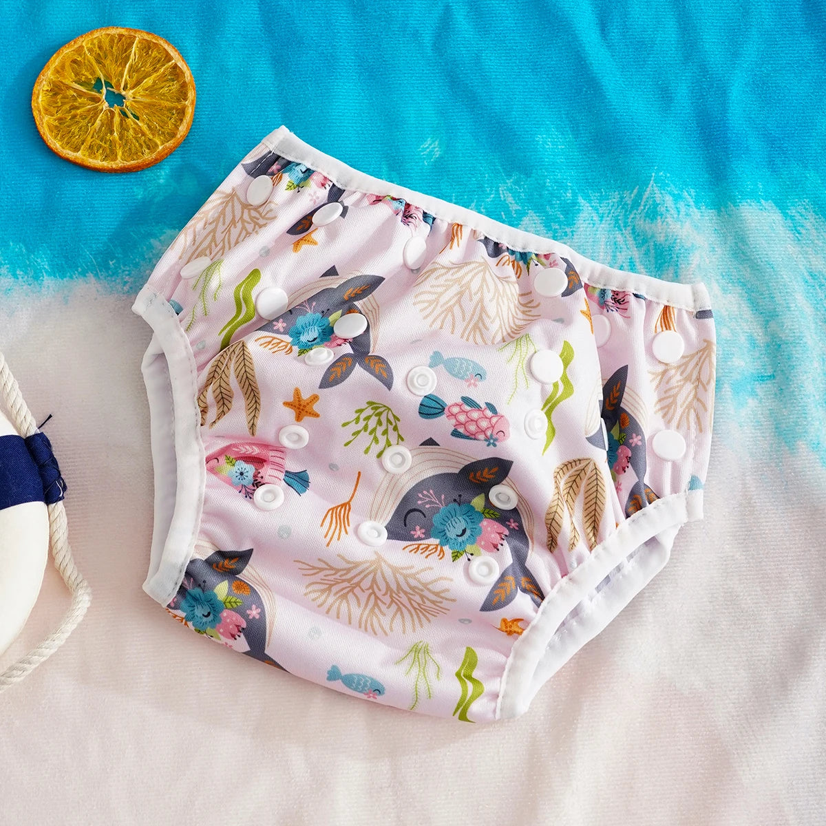 Reusable baby swim diaper in pink with floral whale ocean print and adjustable snap closure for infants.