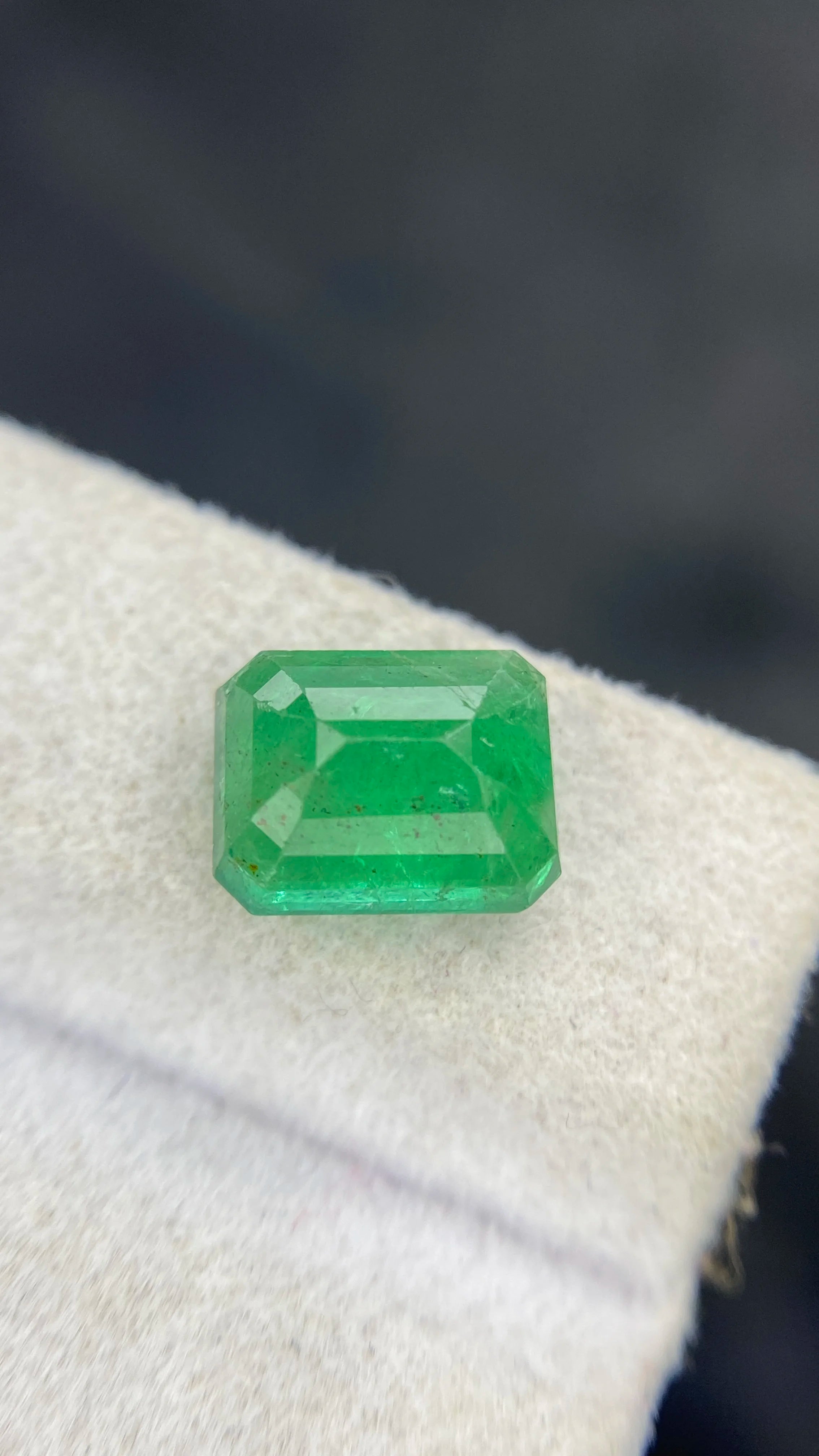 Green emerald-cut gemstone, loose stone with visible step facets on display pad