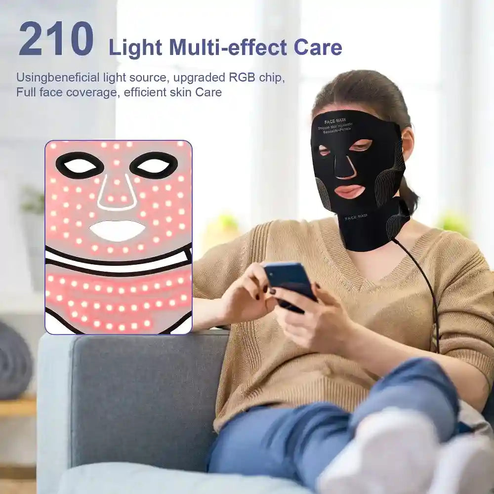 Woman wearing a black flexible silicone LED face and neck therapy mask while using a smartphone.