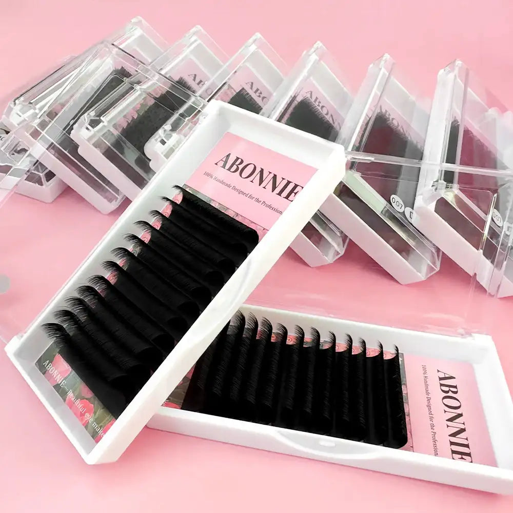 Abonnie cashmere easy fan eyelash extension trays in white cases arranged on a pink background.