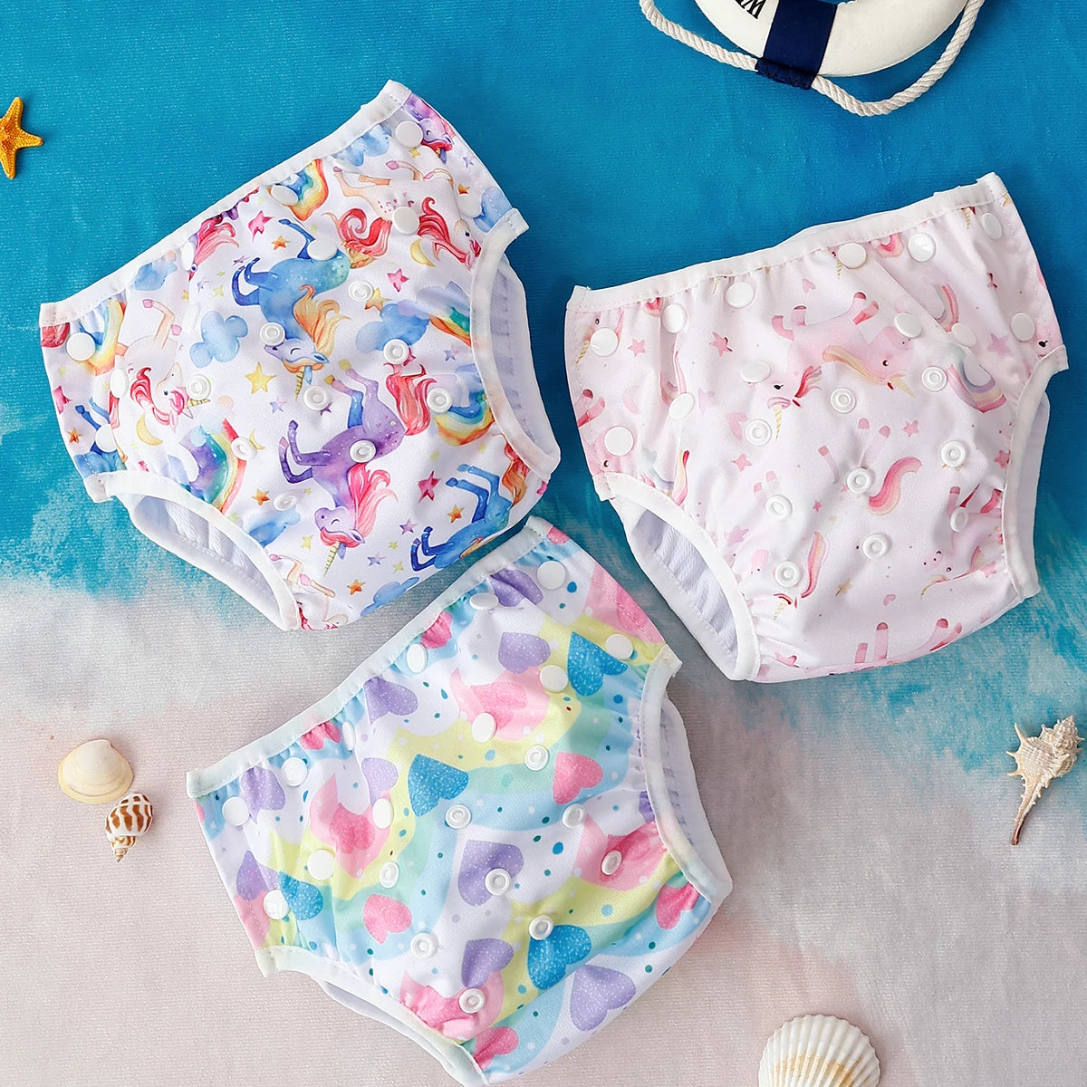 Set of 3 adjustable reusable cloth baby diapers featuring unicorn and heart prints on a beach-themed background.