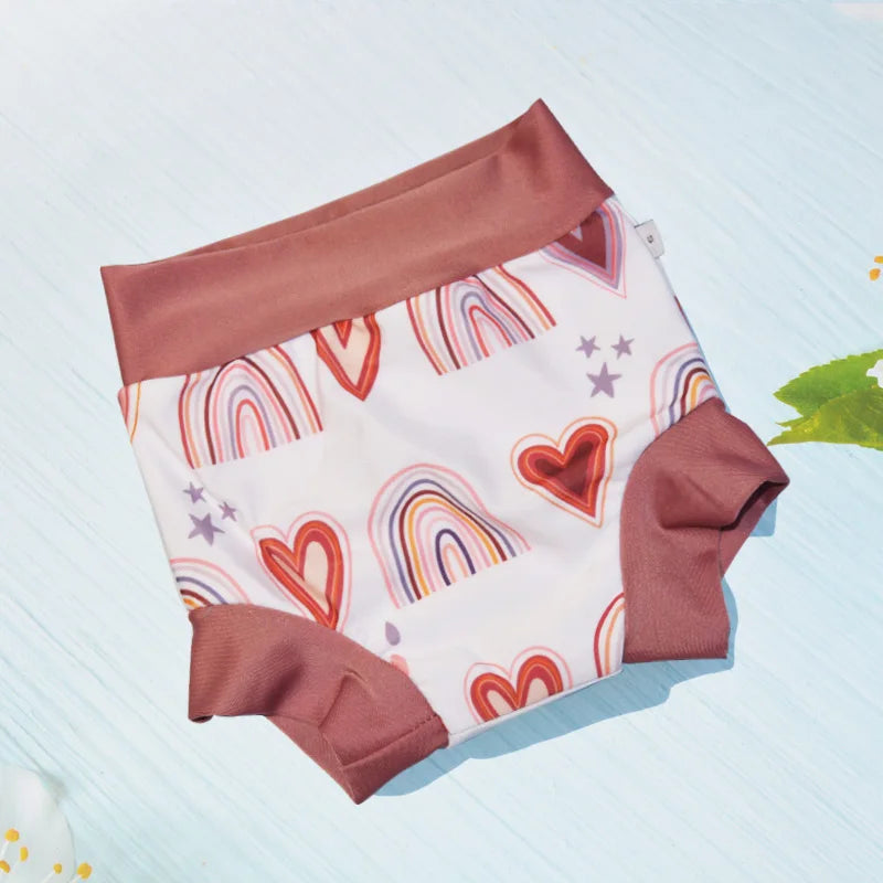 Reusable baby diaper with mauve trim, featuring a cute rainbow and heart print pattern on a light background.