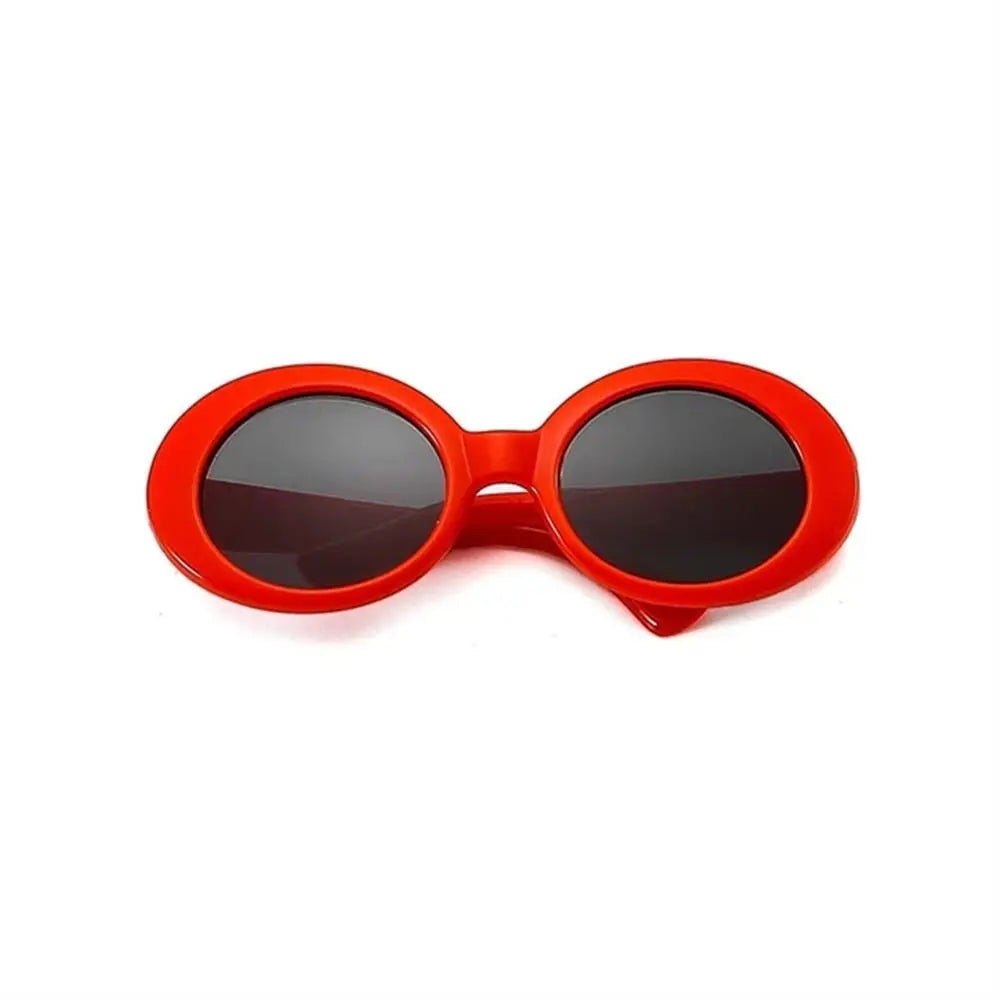 Small bright red oval-shaped plastic doll sunglasses with dark tinted lenses on a plain white background.