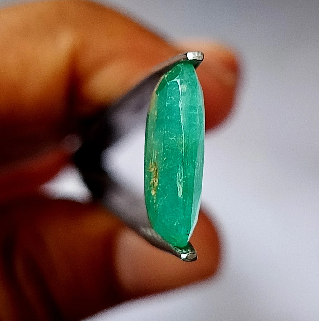 Green oval emerald gemstone, side profile with faceted edges in fingers.